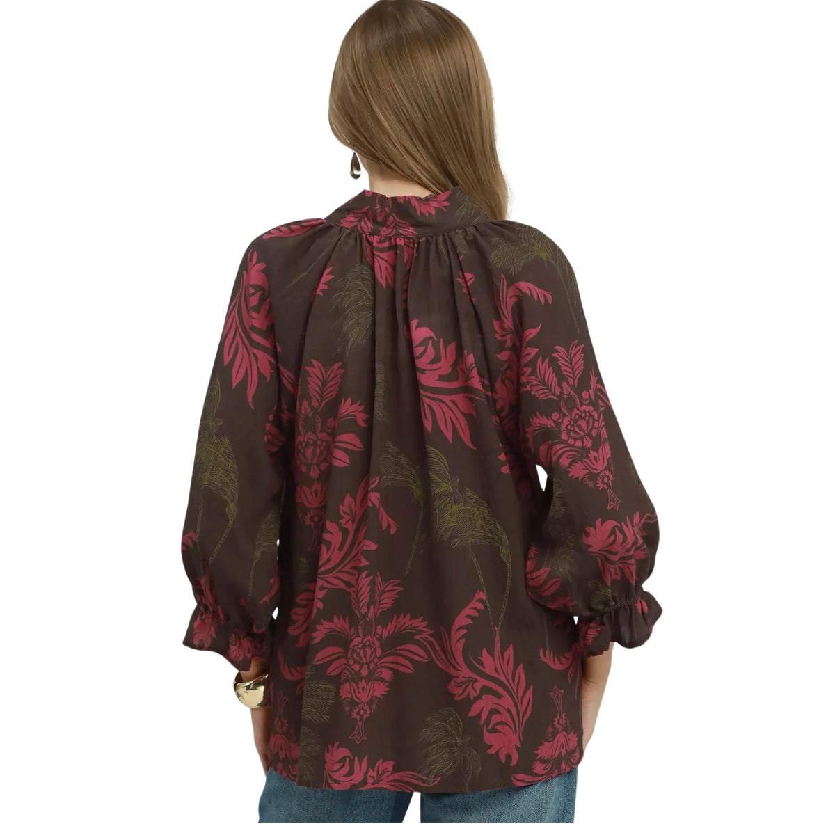 A woman with long brown hair is seen from the back wearing the Umgee Botanical Print Split Neck Blouse by Umgee, which features a loose fit, long sleeves, and a red and green floral pattern.