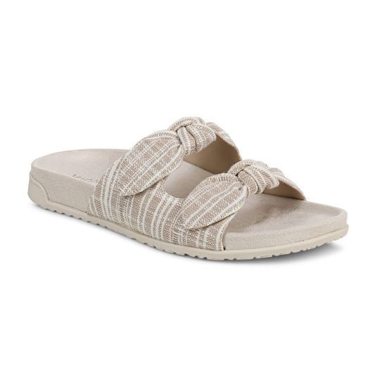 The Vionic Elara Adjustable Slide Sandal features two wide, textured beige fabric straps with knot details and a contoured supportive sole for comfort.