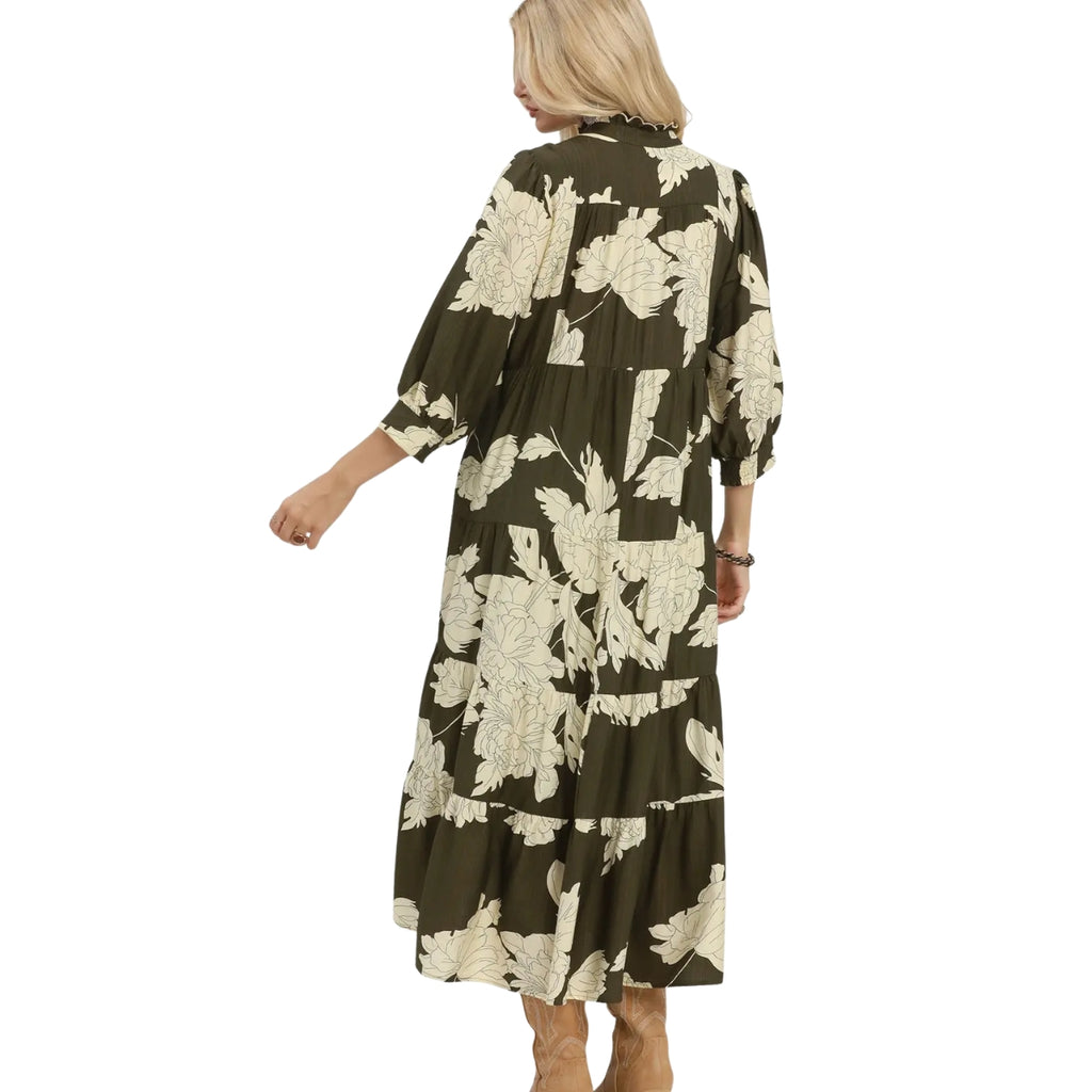A person is seen from behind wearing the Umgee Floral Tiered Maxi Dress, which features long sleeves, an ankle-length cut, and a dark green color with large white floral prints.