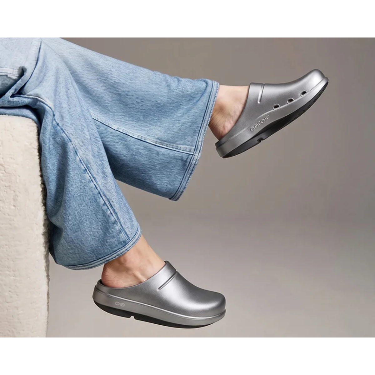 A person wearing metallic gray Womens’ Clog Cloog Luxe by Oofos in Basalt recovery clogs with a thick black sole.