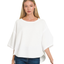 A woman wearing the Zenana Double Knit Exposed Seam Curved Hem Top with wide sleeves and blue jeans stands against a white background.