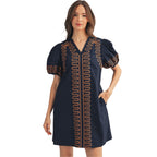 A woman wearing the FASHION GO Short Puff Sleeves Embroidered Shift Dress—navy blue cotton with puff sleeves and orange wavy trim details—stands against a plain background, one hand in her pocket.