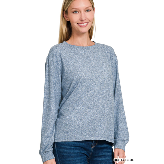 A woman wearing the Zenana Soft Melange Hacci Round Neck Long Sleeve Tee in dusty blue with blue jeans stands and smiles against a plain white background.