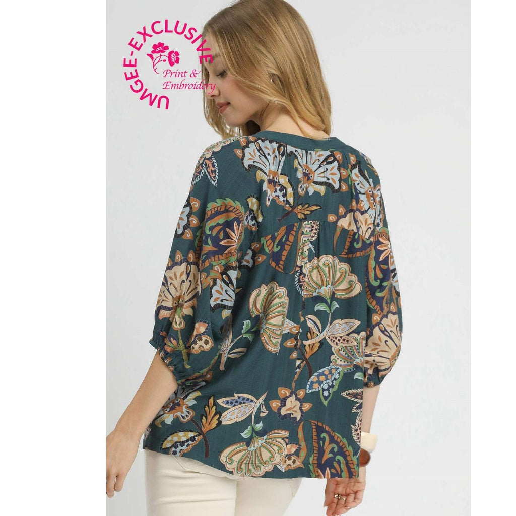 A woman is shown from the back wearing the Umgee Boho Paisley Puff Sleeve Blouse, a dark green top featuring a floral paisley print and three-quarter puff sleeves. The “EXCLUSIVE Print & Embroidery” stamp appears in the upper left corner.