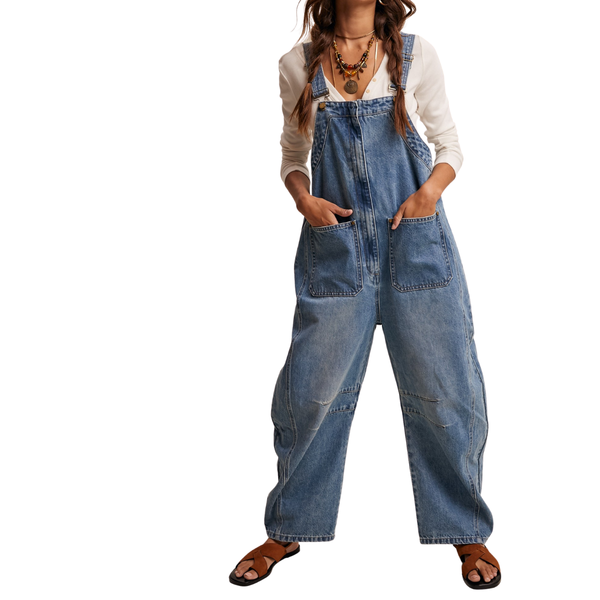 Model wears FASHION GO Barrel Leg Denim Overalls in a sunwashed blue wash, featuring a loose, relaxed fit. Styled with a white long-sleeve shirt, layered necklaces, and sandals; hands in pockets against a white background.