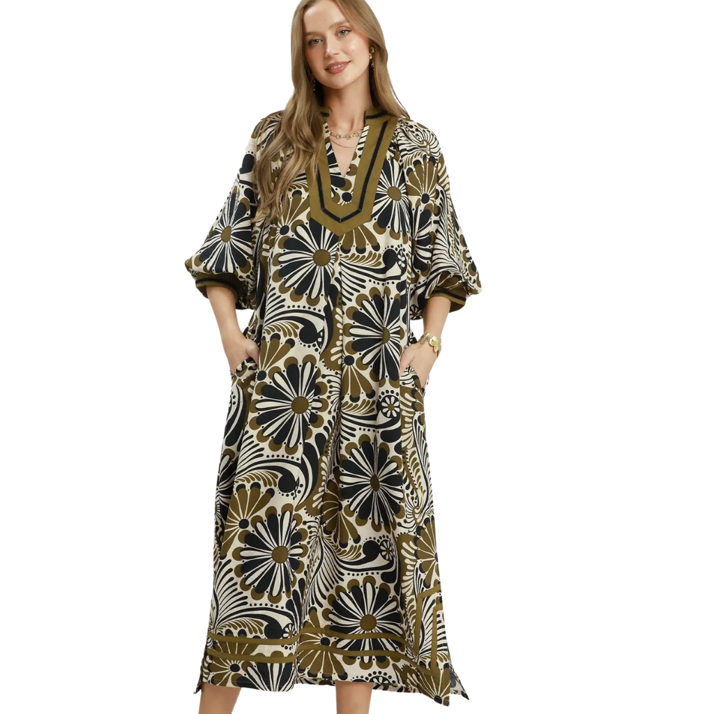 A woman models the Umgee Abstract Print Midi Dress featuring black, white, and olive green floral designs with pockets. The flowy midi silhouette brings effortless style against a white background.