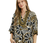 A woman wears the Umgee Abstract Print Midi Dress, featuring a flowy silhouette, abstract black, white, and olive green designs, and a V-neckline with decorative trim.