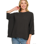 A woman wearing the FASHION GO Double Knit 3/4 Sleeve Top in black and blue jeans, smiling with one hand touching her hair, stands against a white background.