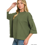 A woman is wearing the FASHION GO Double Knit 3/4 Sleeve Top in an oversized, ribbed olive green style, paired with blue jeans and posing against a white background.