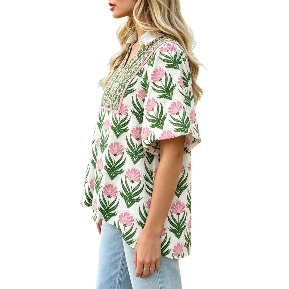 A woman stands sideways against a white background, wearing light blue jeans and the Fahiongo Floral Print Puff Sleeve Contrast Bordered V-Neck Blouse—a short-sleeve, white blouse adorned with a pink and green floral pattern.
