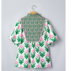 The Fahiongo Floral Print Puff Sleeve Contrast Bordered V-Neck Blouse features green and pink blossoms, puffed sleeves, a contrasting patterned yoke, and a flattering V-neckline, displayed on a hanger against a light gray wall.