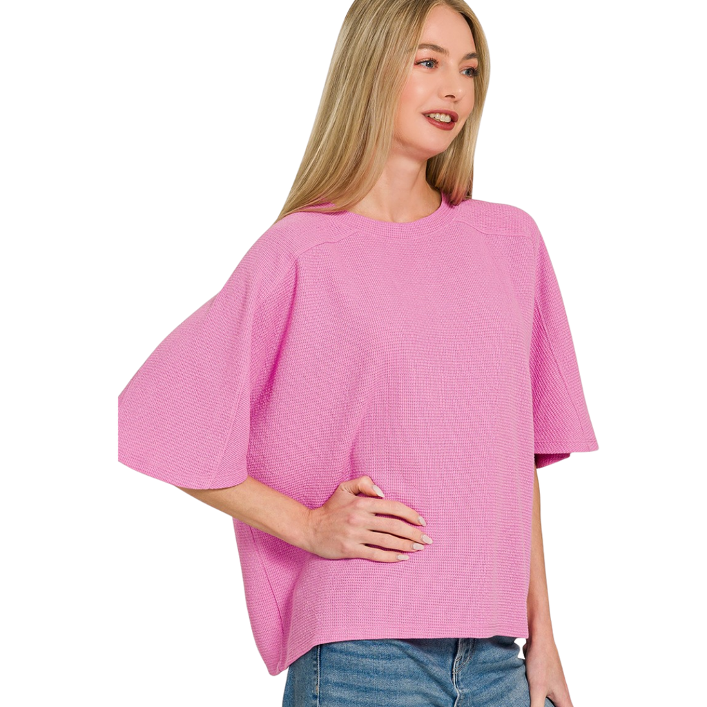 A woman wears the Zenana Double Knit Short Sleeve Top in pink and blue jeans, posing with one hand on her hip against a white backdrop—a comfortable choice for everyday essentials.