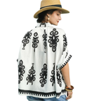 A woman with a braid is seen from the back wearing an Umgee Abstract Print Top—white with black florals—styled with a straw hat and accessorized wrists for an effortlessly oversized look.
