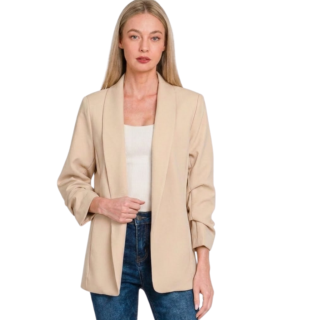 A woman models the Zenana Woven 3/4 Ruched Sleeve Open Front Classic Blazer in beige, styled over a white top and blue jeans, standing against a white background.