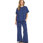 A woman wears the Zenana Scuba Curved Hem Top & Pants Set, a matching loungewear outfit, and smiles while standing against a white background.