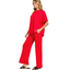 A woman stands in profile wearing the Zenana Scuba Curved Hem Top & Pants Set—a loose-fitting red top with curved hem and matching wide-leg pants—with hands in pockets and black sandals.