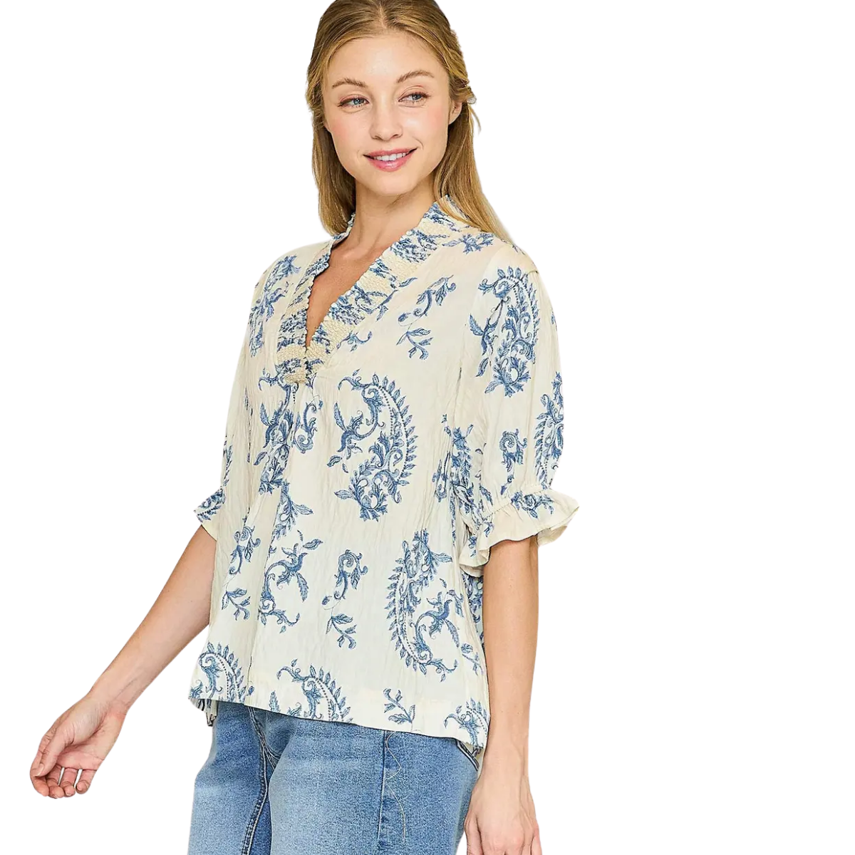 A woman smiles to the side in the Umgee Willow Vine Ruffle Trim Blouse—cream with blue floral patterns, 3/4 puff sleeves, and a notched V-neckline—paired with blue jeans against a white background. Main image