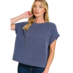 A woman in the Zenana Raised Rib Cap Sleeve Top, featuring a loose fit and boat neckline with blue stripes, paired with dark jeans, stands with one hand in her hair.