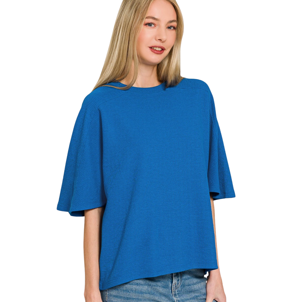 A woman with long blonde hair wears Zenana Double Knit Short Sleeve Tops with blue jeans, standing against a white background.