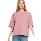 A woman wears the Zenana Double Knit Short Sleeve Top in light pink with a ribbed texture and blue jeans, standing against a white background—an ideal choice for everyday essentials.