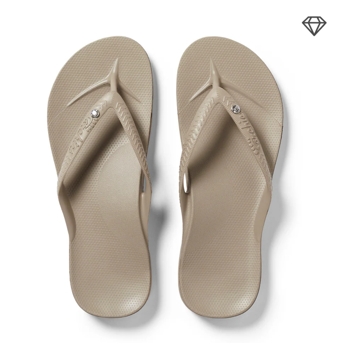 The Archies Arch Support Flip Flops Crystal Taupe by ARCHIES FOOTWEAR LLC are shown from above, featuring beige color, textured soles, arch support, and a small crystal detail on each strap against a white background. Main image