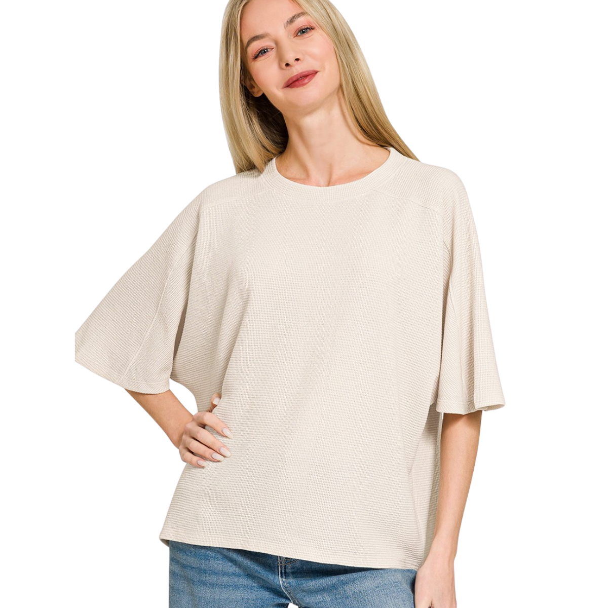 A woman wears a Zenana Double Knit Short Sleeve Top in light beige with blue jeans, standing with one hand on her hip and smiling against a white background.