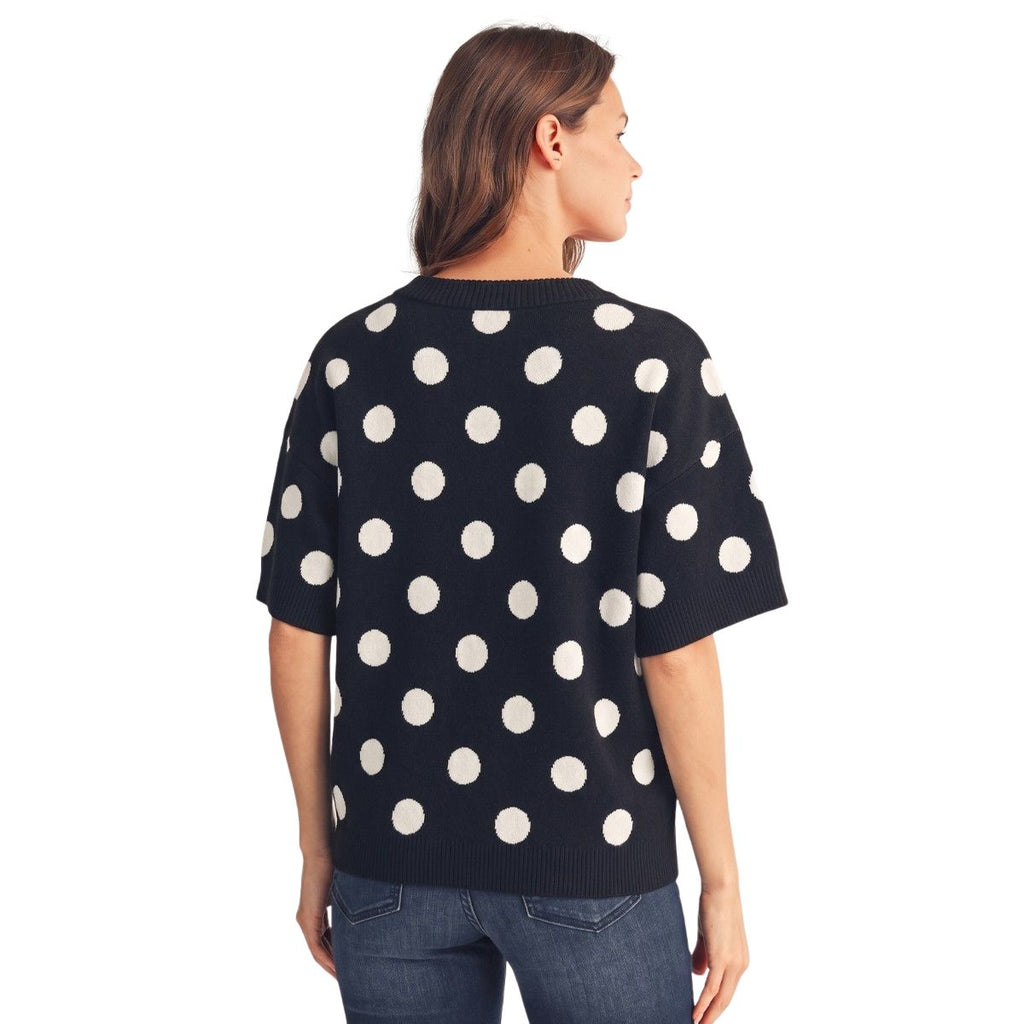 A woman is standing and facing away, wearing the Large Polka Dots Short Sleeve Sweater by FASHION GO—a black and white polka dot sweater with short sleeves.