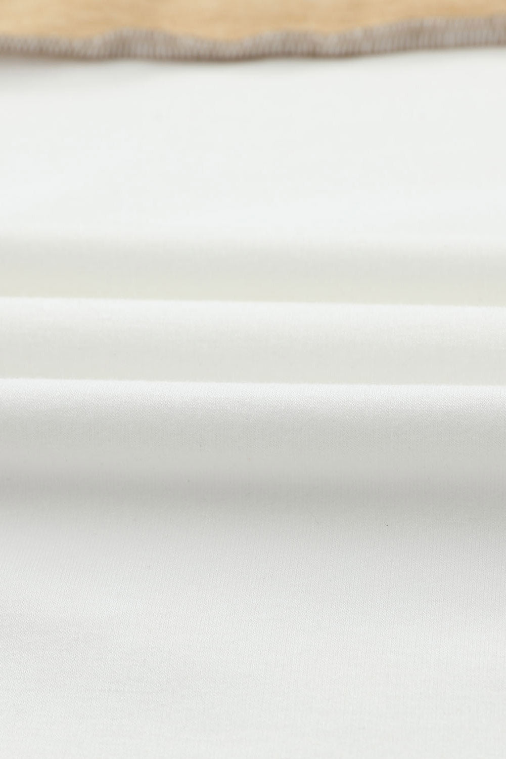 Close-up image of a light-colored fabric with visible folds, lying flat on a surface. The edge of the fabric is visible at the top of the image, showcasing the versatile khaki color of the Shewin Khaki Color Block Exposed Seam Long Sleeve Top.