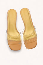The CCOCCI Clear Slip On Slide Block Heel features tan open-toe sandals with clear vinyl straps, square toes, and transparent block heels, shown on a white background.