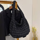 The ACCITY Cloud Tote Bag Large Shoulder Crossbody in black with a quilted design hangs on a wooden rack beside a black blazer; nearby, yellow dried flowers rest on a table.