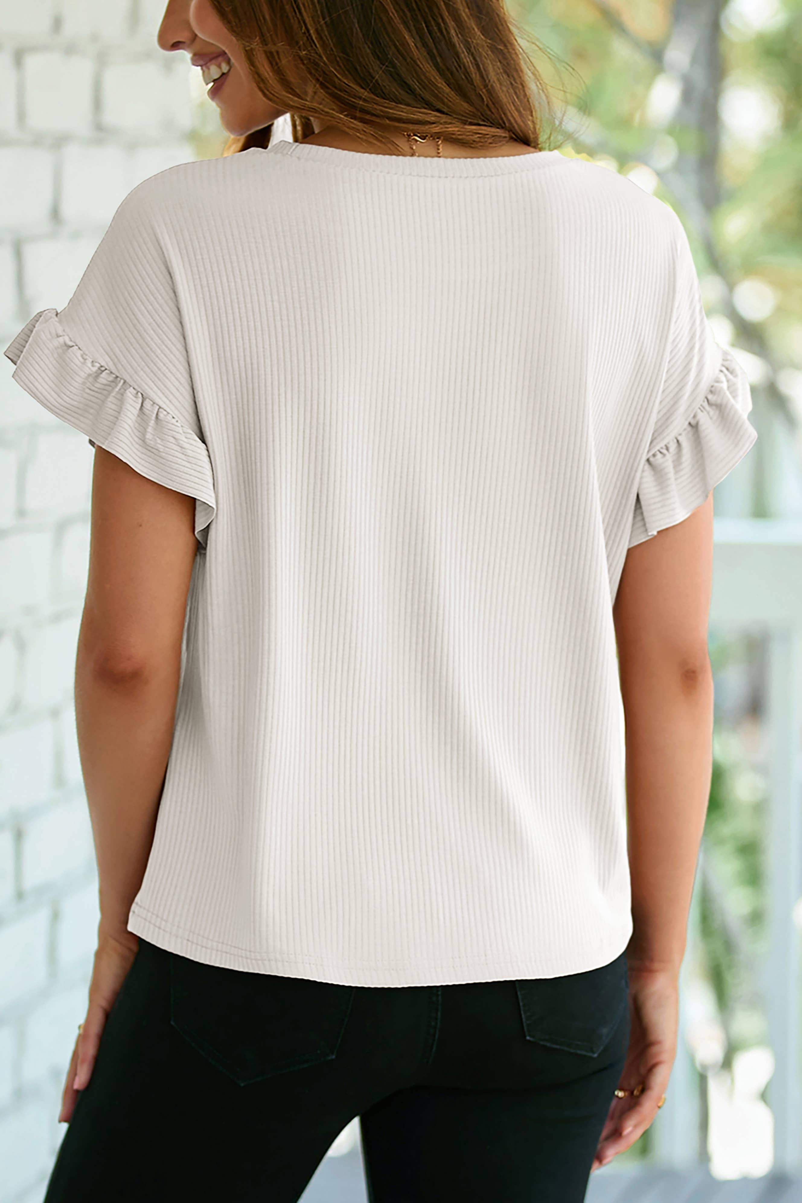 A woman faces away from the camera, wearing the 1 the Woman Solid Color Ribbed Ruffled Short Sleeve T Shirt with black pants.
