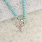 The WJW Stainless Steel Turquoise Chunky Bead Carabiner Necklace features vibrant turquoise beads and a striking silver bull skull pendant accented with a small turquoise stone. Designed for durability, this unique necklace showcases a secure carabiner clasp closure and is beautifully displayed on a light textured surface.