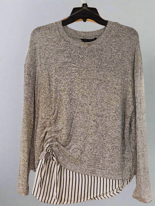 On a wooden display inside a clothing store hangs the Long Sleeve Knit Tunic with Striped Skirting by RONNIE SALLOWAY & CO INC, featuring a gray color and unique striped hem detail that creates a layered look.