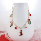 Seasons Jewelry’s Vintage Christmas Charm Necklace features whimsical festive charms—including a stocking, candy cane, gift, ornament, and red beads—displayed on a gold tone chain. Shown draped over a white vase with a red and white background, this vintage-inspired necklace brings playful holiday spirit to any outfit.