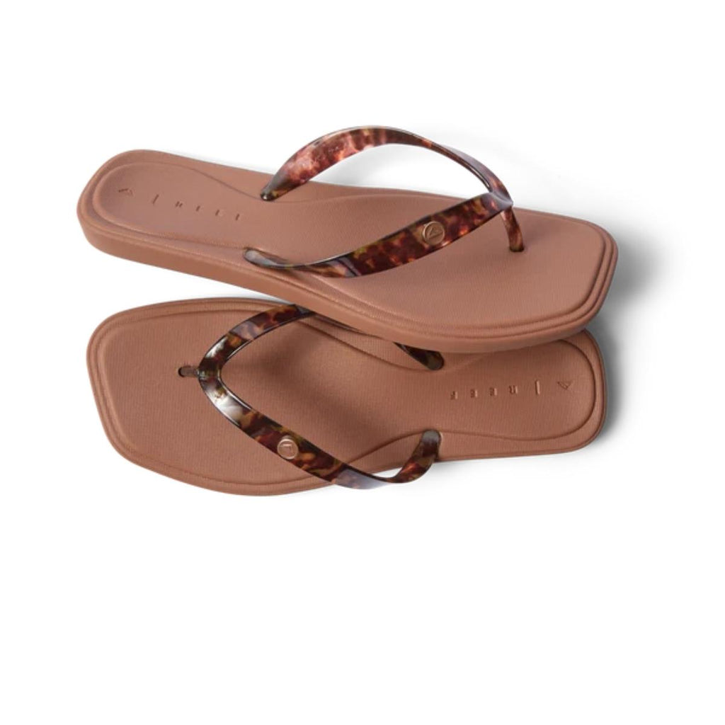 A pair of REEF Solaye Flip Flop in Tortoise, featuring square soles and marbled tortoise-print straps, are placed overlapping on a white background. These water-friendly sandals offer a stylish yet functional option for everyday wear.