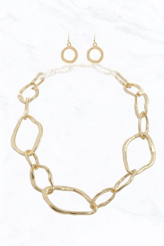 The FASHION GO Irregular Shape Link Statement Necklace features gold-tone large irregular links and matching circular earrings, displayed on a white marble background.