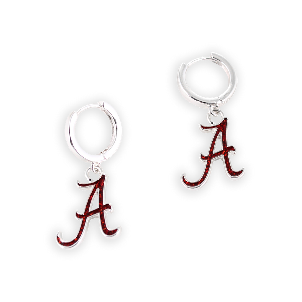 A pair of Alabama Glitter Enamel Logo Huggie Hoop Earrings by Seasons Jewelry features silver huggie hoops, each adorned with a red Alabama “A” logo charm in crimson glitter enamel, dangle elegantly from the hoops and are displayed against a plain white background.
