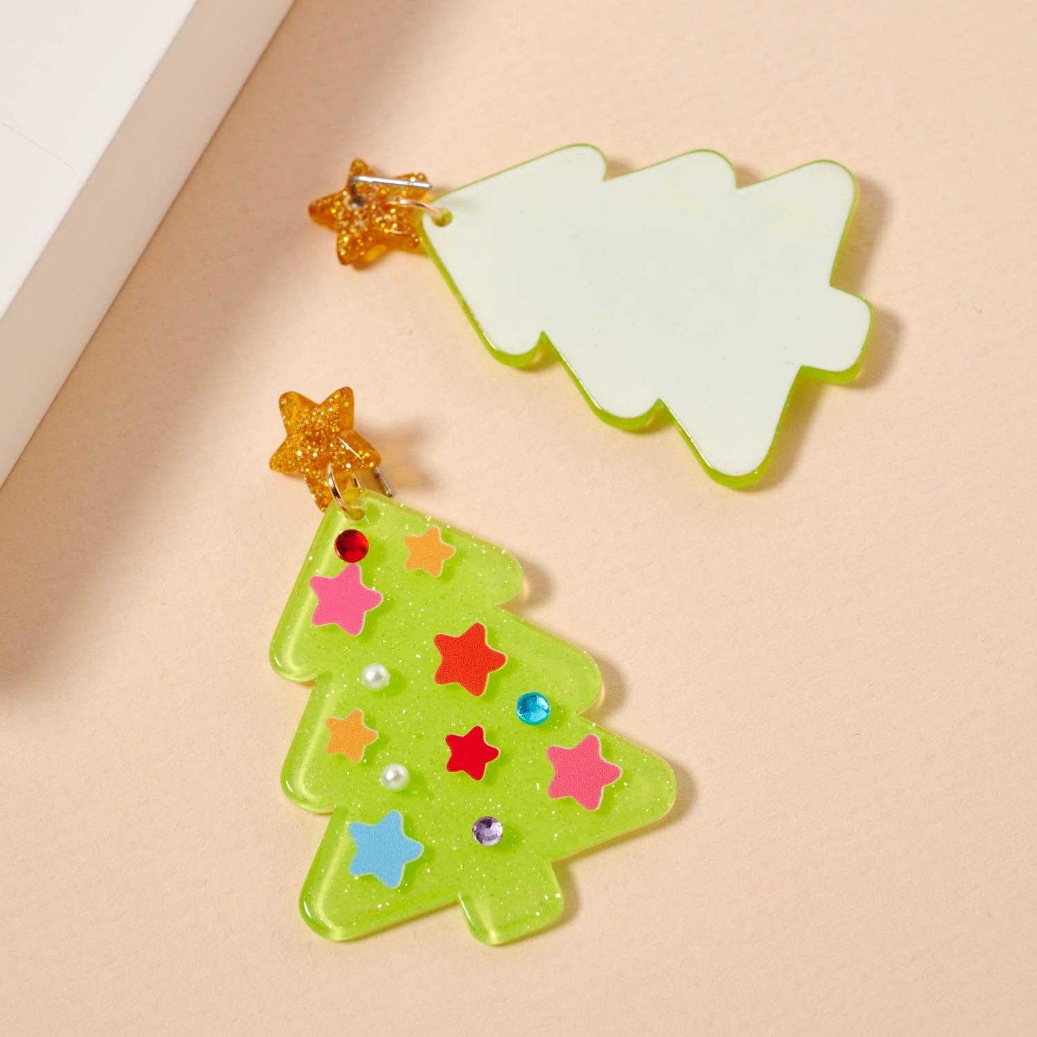 Add festive sparkle to your holiday look with Lilla Haven's Glittery Christmas Tree Drop Earrings—one earring features colorful star and gem accents atop a green tree shape with an orange star topper, while the other remains plain, both crafted in glitter acrylic. Perfect for making a unique seasonal statement!.