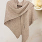 The JC Sunny Fashion Cashmere-Blend Knit Triangle Shawl with Cross-Front Design, in beige, is draped on a wall like a cozy scarf. A large ivory rose is seen in the background on the right.