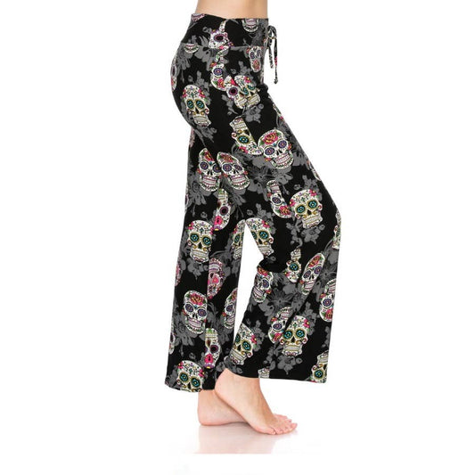 A person models Leggings Depot’s Buttery Soft Print Pajama Pants with a colorful sugar skulls design and an elastic waistband, standing barefoot against a white backdrop.