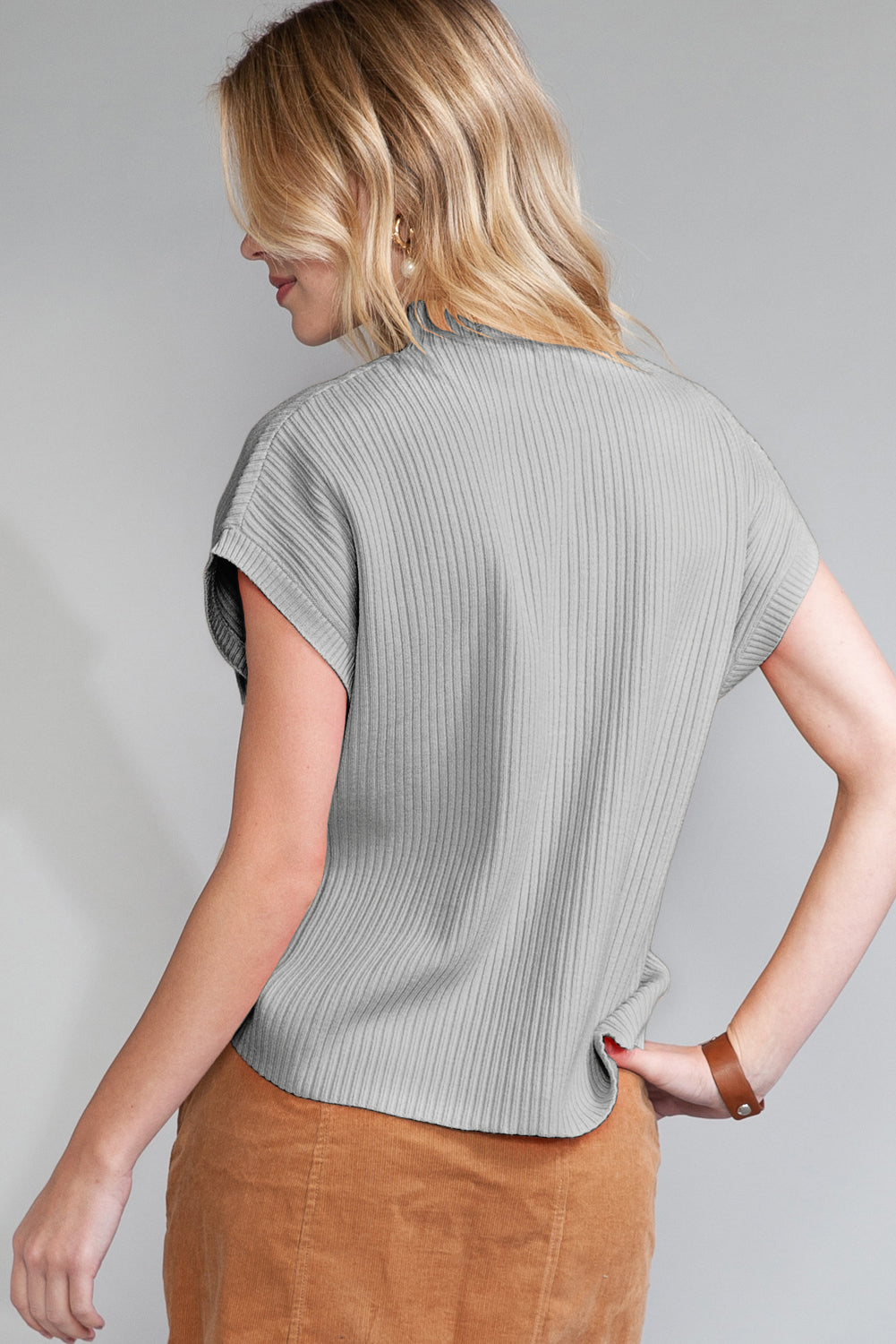 A person wearing Shewin's Patch Pocket Ribbed Knit Short Sleeve Sweater in gray, paired with light brown pants, is facing away from the camera, showcasing an ideal transitional weather look.