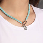 A person wearing a white shirt and the WJW Stainless Steel Turquoise Chunky Bead Carabiner Necklace, featuring a silver rectangular pendant and carabiner clasp detail.