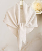 The JC Sunny Fashion Cashmere-Blend Knit Triangle Shawl with Cross-Front Design, in light beige, is displayed on a hanger tied loosely, with a cream rose in the background for chic style.