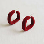 A pair of Ellemadera Retro Geometric Drop Earrings with a bold, red square design and gold posts, displayed on a light-colored fabric background.