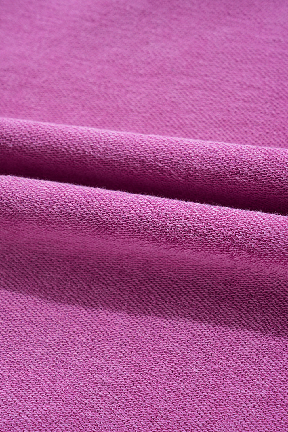 Close-up of folded magenta fabric with a textured surface, similar to the Shewin Notched Neck Exposed Seam Drop Shoulder Sweatshirt crafted from high-quality material.