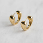 A pair of Contemporary Geometric Drop Earrings by Ellemadera, featuring a small gold heart-shaped hoop design displayed on a white fabric surface—perfect for adding a touch of modern jewelry style to any look.