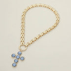 Here’s a revised sentence using your product data: The Pearl Cross Charm Pendant Chunky Chain Statement Necklace by Sensibling Corp. features a bold gold chain and a textured cross pendant adorned with six round blue gemstones, creating a striking statement piece.