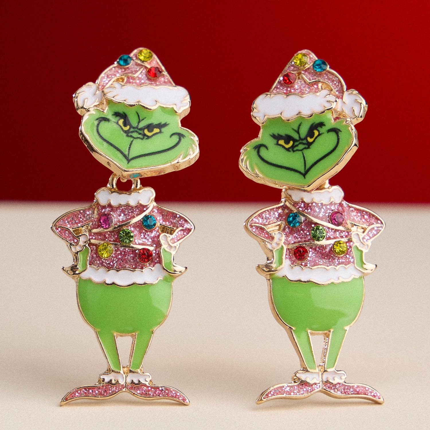 Add a playful touch to your holiday style with the Enamel Green Monster Drop Earrings from Lilla Haven—festive earrings shaped like the iconic green character in a Santa hat, decorated with colorful rhinestones and Christmas lights, perfect for whimsical seasonal flair. Main image