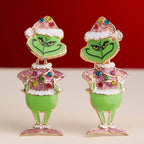 Add a playful touch to your holiday style with the Enamel Green Monster Drop Earrings from Lilla Haven—festive earrings shaped like the iconic green character in a Santa hat, decorated with colorful rhinestones and Christmas lights, perfect for whimsical seasonal flair.