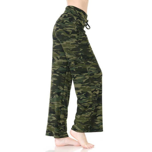 A person stands barefoot against a plain white background wearing Leggings Depot Buttery Soft Print Pajama Pants in a loose-fitting green camouflage pattern with an elastic waistband.